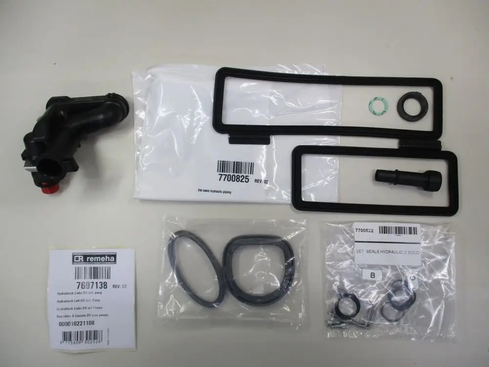 Hydraulikkomponenten von Remeha, bestehend aus einem schwarzen Hydroblock, Dichtungen und weiteren Zubehörteilen, auf einem neutralen Untergrund angeordnet.